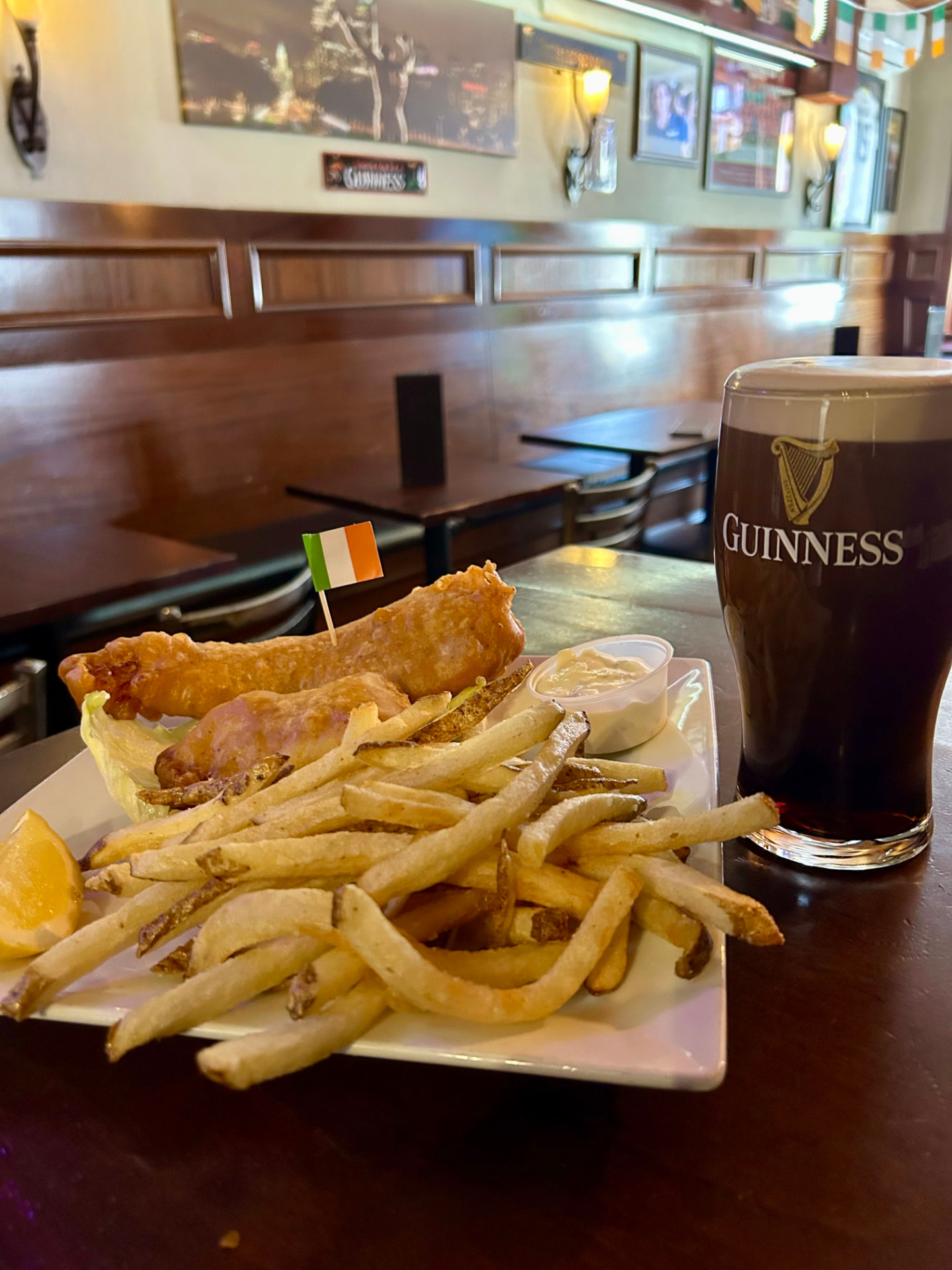 Fish and chips with an Irish flag toothpick, a lemon wedge, tartar sauce and a pint of Guinness on a pub table