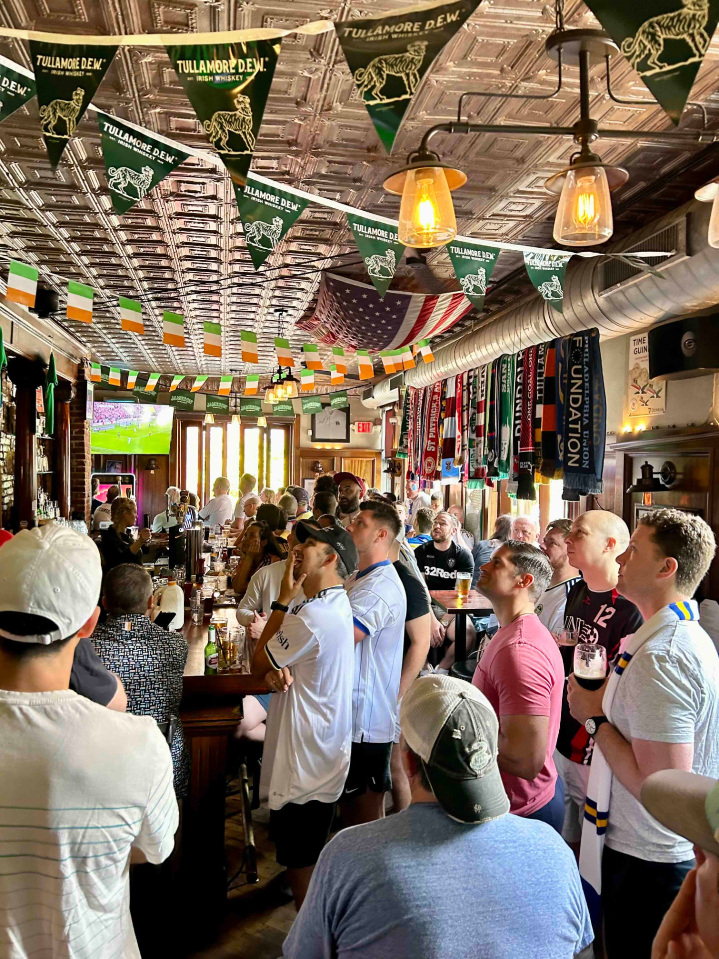 A packed pub on match day, fans watching soccer beneath Irish flags and scarves